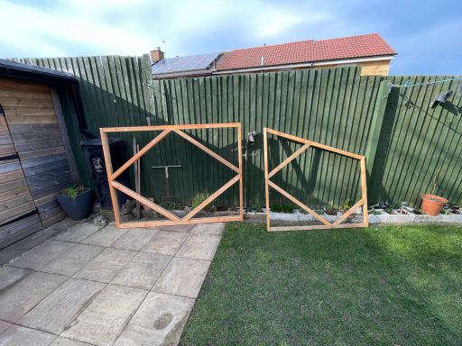 Wooden fence frames created in different shapes in front of a green fence in a garden